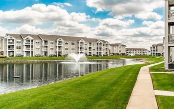 A row of apartment buildings are lined up next to a pond with a fountain in the middle